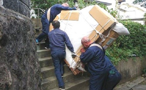 石段で3人のスタッフが梱包されたピアノを運んでいる様子